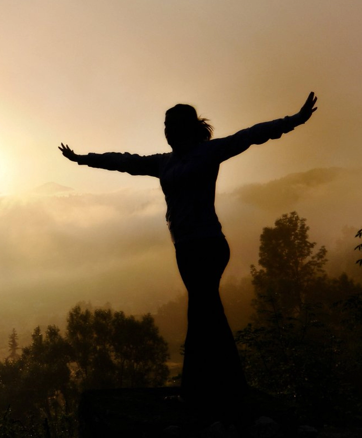 BST Projekt-Bau GmbH - Badezimmersanierung - Eine Person steht bei Sonnenaufgang mit ausgestreckten Armen vor einer dunstigen Bergkulisse.